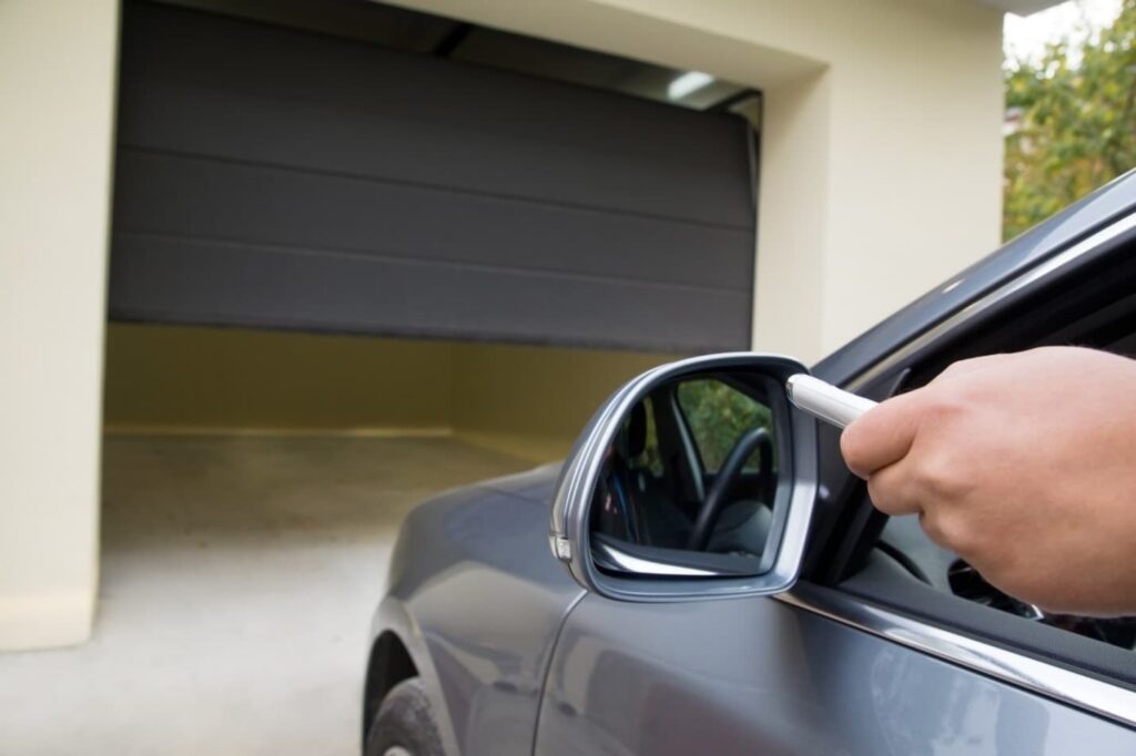 man driving his car into his garage using a remote to open the door